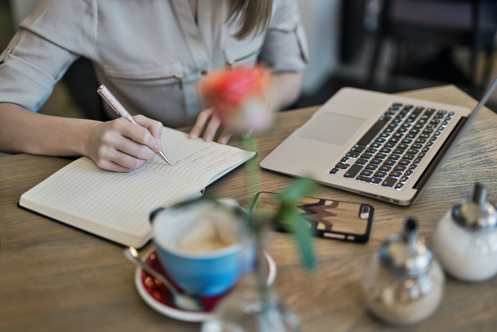 Woman writing on a notebook with laptop on desk
